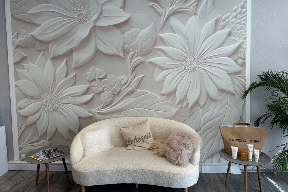Gemütlicher Wartebereich im Beautyfashion Nagel- und Kosmetikstudio Odelzhausen mit Sofa, Kissen und dekorativer Blumenwand.